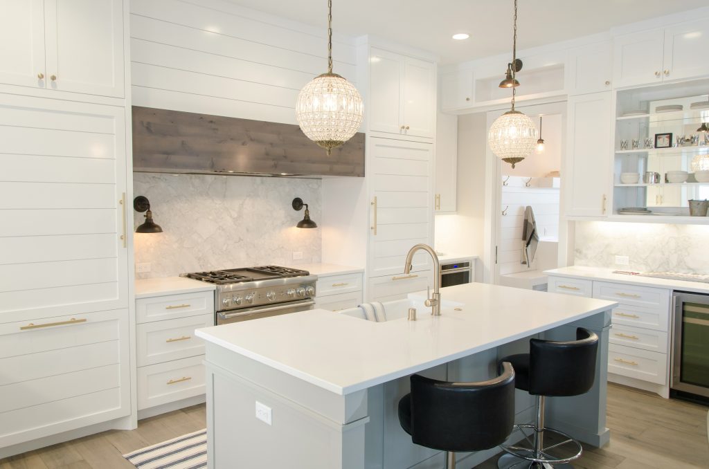 Modern farmhouse kitchen remodel in Beverly Hills, California, by SK Home Designs featuring crystal globe pendants, a marble backsplash, and white shaker cabinetry.