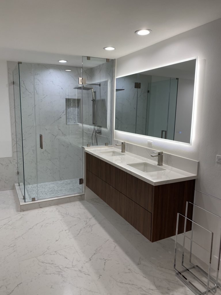 Modern master bathroom in Century City featuring a floating walnut double vanity, backlit LED mirror, frameless glass walk-in shower with marble tile, and large-format porcelain flooring.
