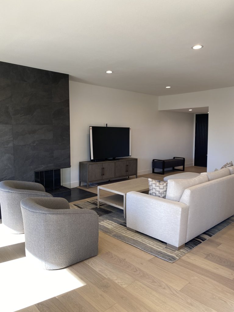 Modern Los Angeles living room featuring a floor-to-ceiling charcoal slate fireplace, light oak hardwood flooring, and minimalist neutral furniture for a 2026 home expansion project.