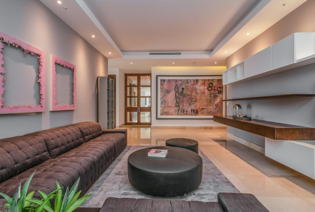 Modern living room design in Santa Monica, California, by SK Home Designs featuring custom pink pop art frames, a brown tufted sofa, and minimalist walnut shelving.