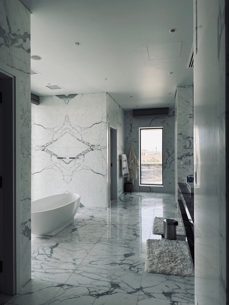 Luxury modern marble bathroom remodel featuring a freestanding soaking tub and matching marble wall-cladding designed by SK Home Designs and Remodeling.