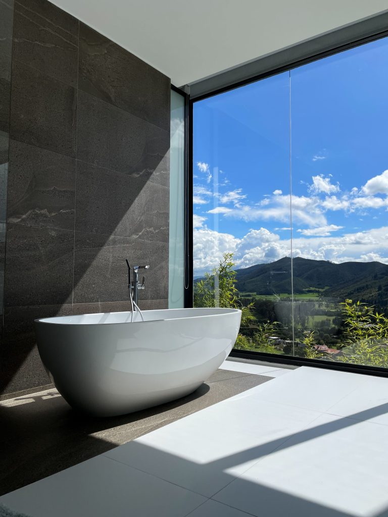 Luxury bathroom renovation in Southern California featuring a freestanding oval soaking tub, large-format dark stone feature wall tile, and floor-to-ceiling windows — by SK Home Designs & Remodeling